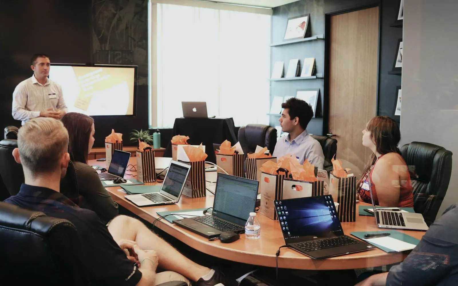 A sales lead presenting to a team seated around a table with laptops