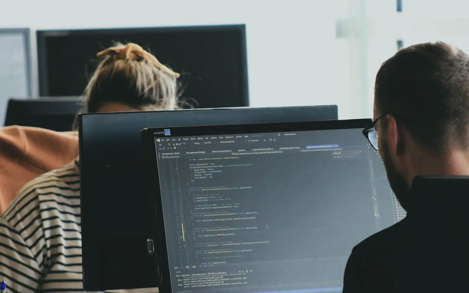 Two engineers working through code on their monitors in a bright office